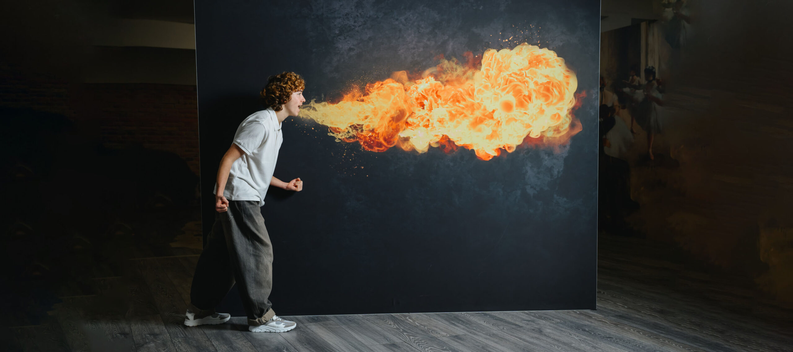Teenage boy with curly hair in a white polo, baggy jeans, and GIGAshoes white and grey sneakers, pretending to breathe fire in front of a dark backdrop in a street setting.
